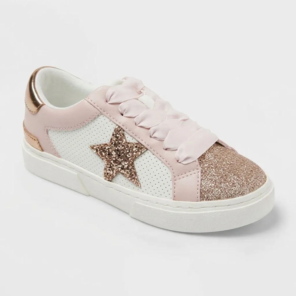 A low-top sneaker for kids featuring a light pink leather upper, white perforated side panels, a glittery rose gold star on the side, a matching glittery rose gold toe cap, and a white rubber sole.