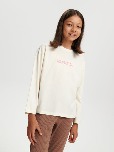 Person wearing a white sweater with pink text on a plain background