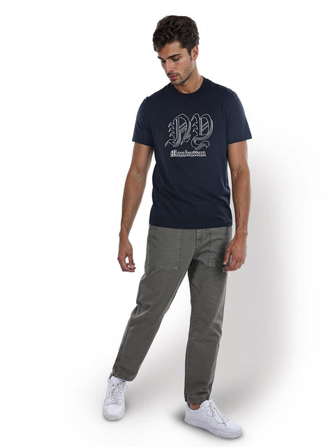 Man wearing a navy t-shirt with a logo and gray pants on a white background
