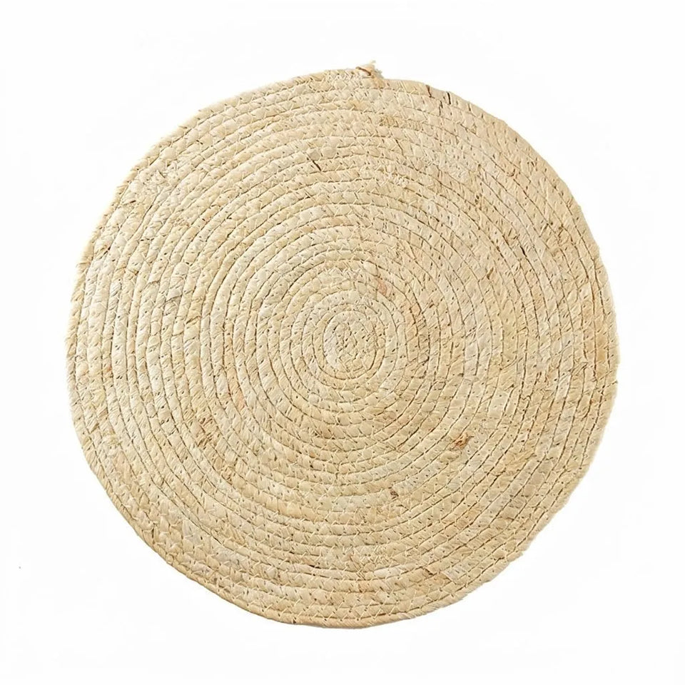 A round natural woven placemat made from seagrass or straw, featuring concentric spiral patterns, shown on a solid white background.