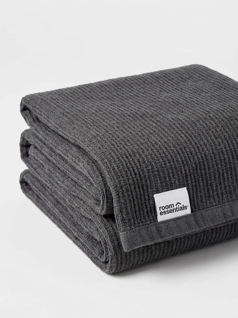 A folded dark gray ribbed blanket with a white 'room essentials' brand tag, shown on a clean light gray background.
