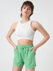 Woman wearing a white sleeveless top and green shorts on a light gray background