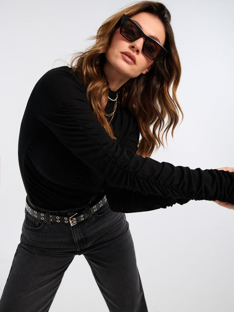 Woman wearing a black long-sleeve top and black pants with sunglasses on a white background