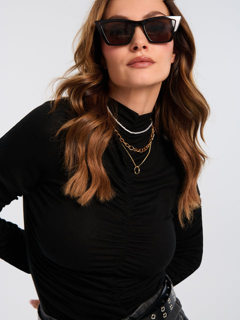 Woman wearing sunglasses and a black outfit with layered necklaces on a plain background