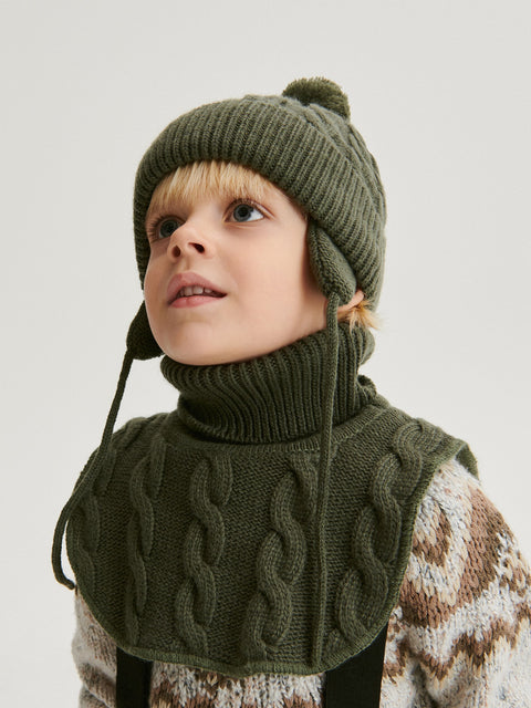 Child wearing a green knitted hat and scarf on a light background