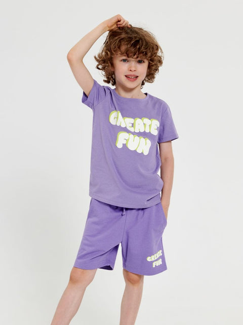 A boy wearing a purple short-sleeve t-shirt with text on it and matching purple shorts.