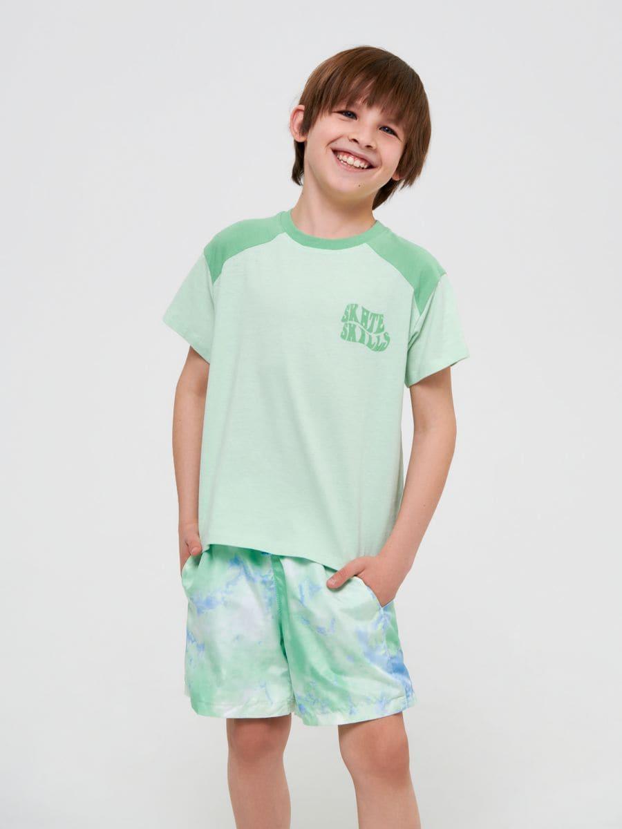 Child wearing a green t-shirt and shorts with a logo on a white background
