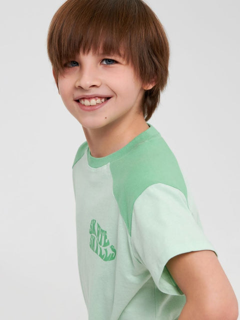 Child wearing a light green t-shirt with a logo on a plain background