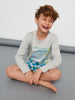 Child sitting on a gray surface wearing a gray long-sleeve shirt and blue shorts with graphic design.