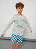 Child wearing a gray long-sleeve shirt with colorful text and blue checkered shorts on a plain background