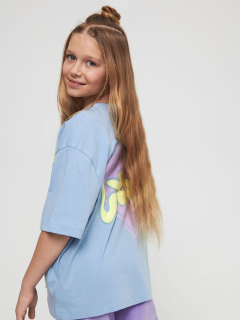 Young girl wearing a light blue t-shirt with a colorful design on a plain background