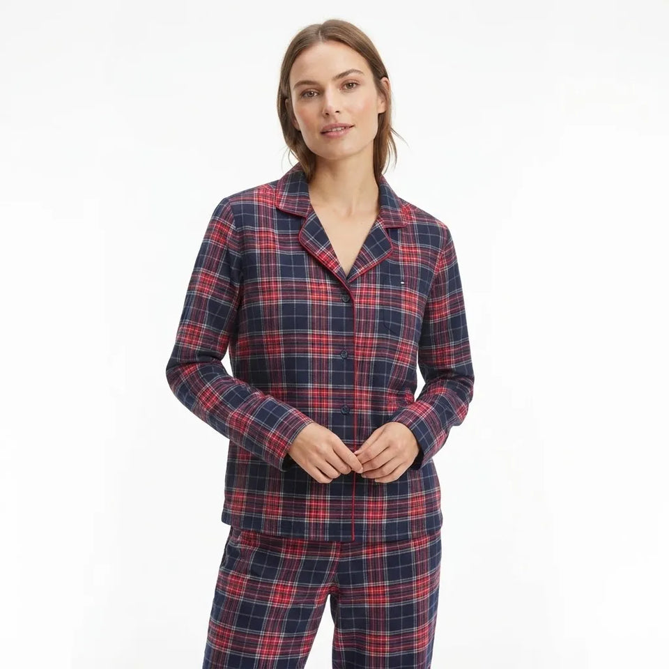 A woman modeling a matching long-sleeve button-front pajama top and pants set in a navy blue and red plaid pattern, photographed against a clean white studio background.