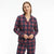 A woman modeling a matching long-sleeve button-front pajama top and pants set in a navy blue and red plaid pattern, photographed against a clean white studio background.