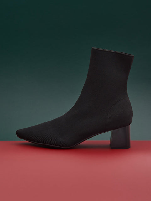Black ankle boot on a red platform with a green background