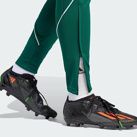 Person wearing green tracksuit and black Adidas soccer cleats on a white background