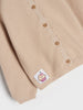 Beige cardigan with a small patch featuring a cartoon cupcake design on a white background