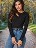 Woman wearing a black long-sleeve top and blue jeans standing outdoors with trees in the background.
