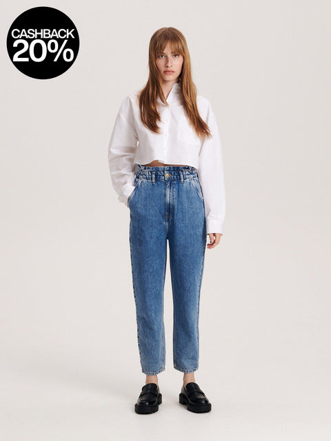 Person wearing blue jeans and a white shirt on a light gray background with a cashback 20% badge.