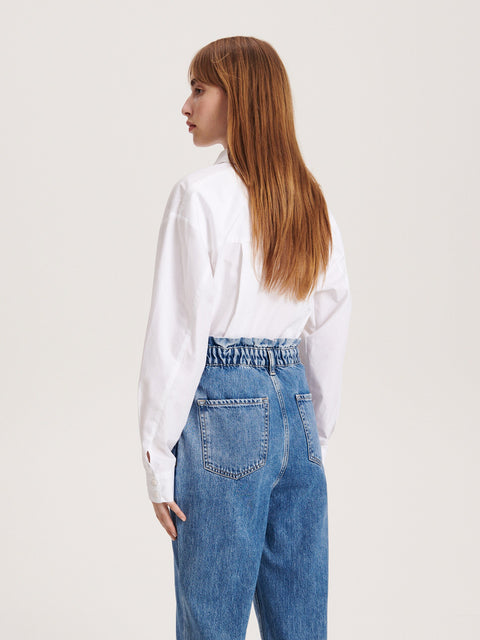 Person wearing a white shirt and blue jeans on a plain background