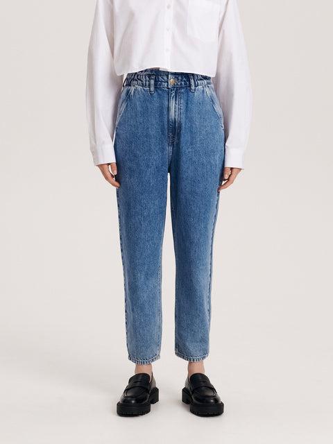 Person wearing blue jeans and a white shirt on a plain background