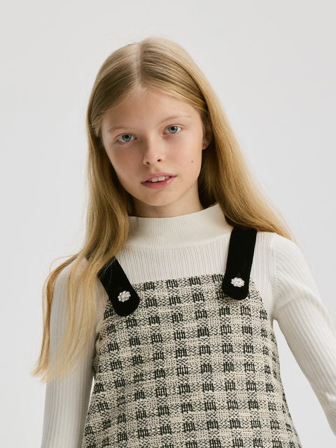 Young girl wearing a patterned dress with black straps against a white background