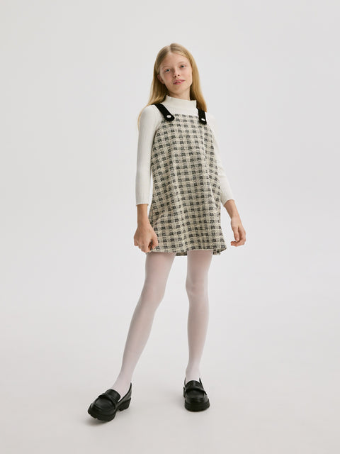 Young girl wearing a checkered pinafore dress on a white background