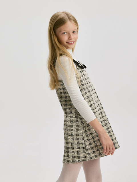 Young girl wearing a checkered dress with a white shirt underneath on a light gray background