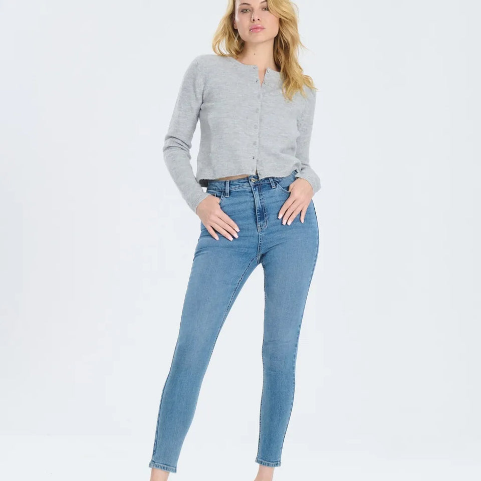 A woman modeling a light gray long-sleeve cropped cardigan and medium-wash blue skinny jeans against a plain white studio background.