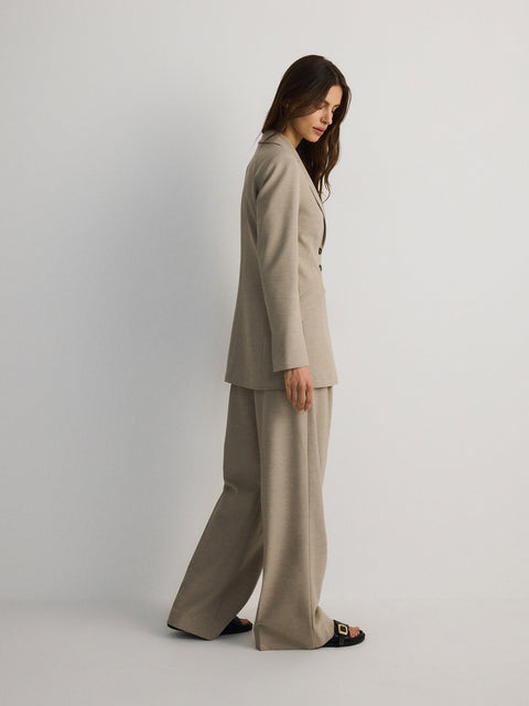 Woman wearing a beige suit standing against a plain background