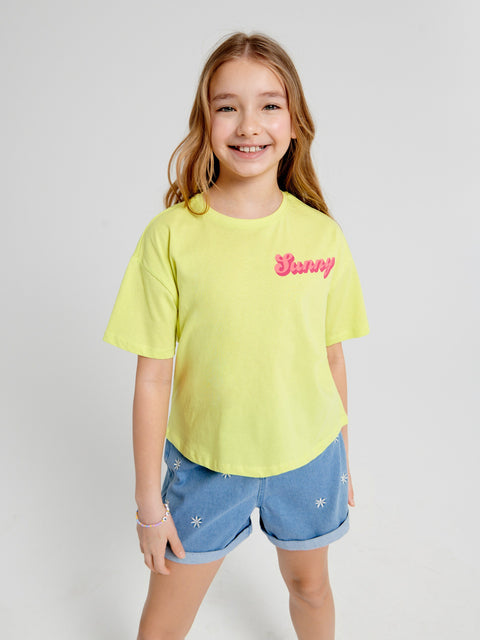 Young girl wearing a yellow t-shirt with 'Sunny' text and blue shorts on a white background