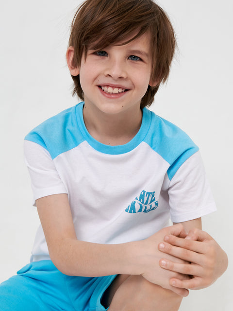 Child wearing a blue and white shirt with text, sitting on a white background