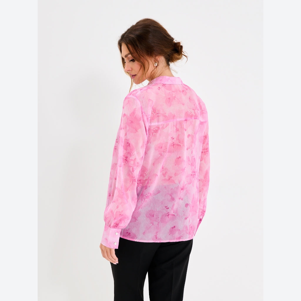 A woman wearing a pink long-sleeve button-up shirt with a watercolor-style pink pattern, shown from the back against a plain light gray studio background.