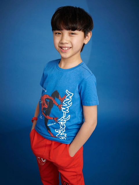 Child wearing a blue t-shirt with a graphic design and red pants against a blue background
