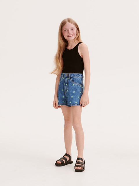 Young girl wearing a black tank top and blue denim skirt on a white background