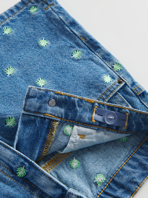 Close-up of blue denim jeans with floral embroidery on a light gray background