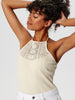 Woman wearing a beige sleeveless top with lace details against a white background