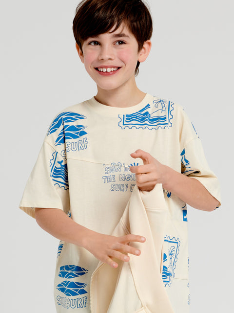 Child wearing a cream-colored outfit with blue graphics and text on a plain background