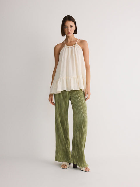 Woman wearing a white top and green pants on a plain background