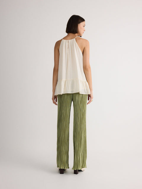 Woman wearing a white top and green pants on a plain background