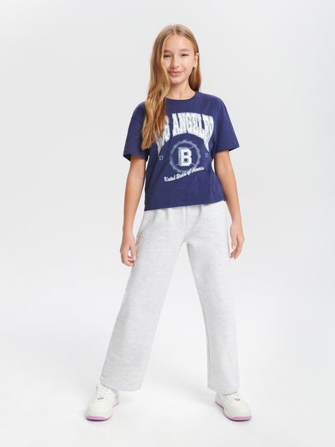 Person wearing a blue t-shirt with a logo and white pants on a light gray background