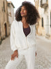 Woman in a white jacket and pants walking down a street.