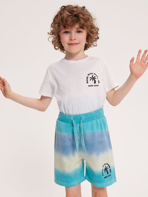 Child wearing a white t-shirt and blue tie-dye shorts with a logo on a light gray background