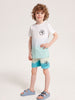 Child wearing a white t-shirt and blue shorts with a palm tree design on a plain background