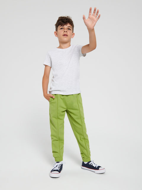 Child wearing a white t-shirt and green pants waving on a white background