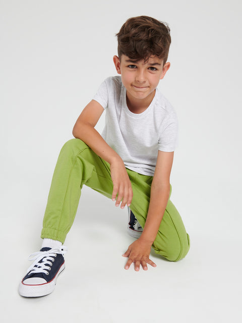 Child wearing a white t-shirt, green pants, and blue sneakers on a white background