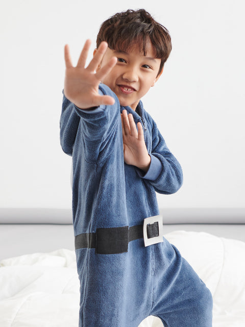 Child wearing a blue onesie with a belt, standing on a white surface.