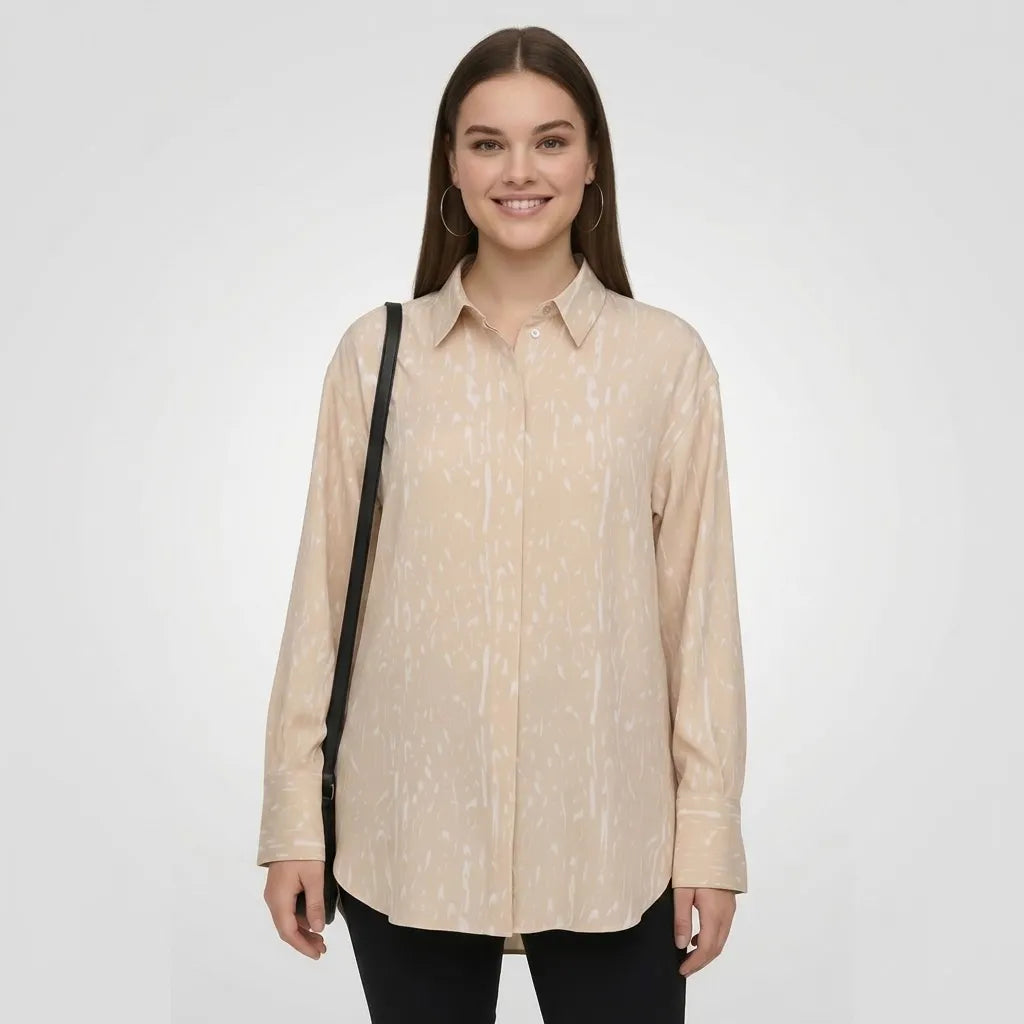 A woman modeling a light beige long-sleeve button-up shirt with a subtle white vertical streak pattern, paired with black pants and a black shoulder bag, against a light gray studio background.