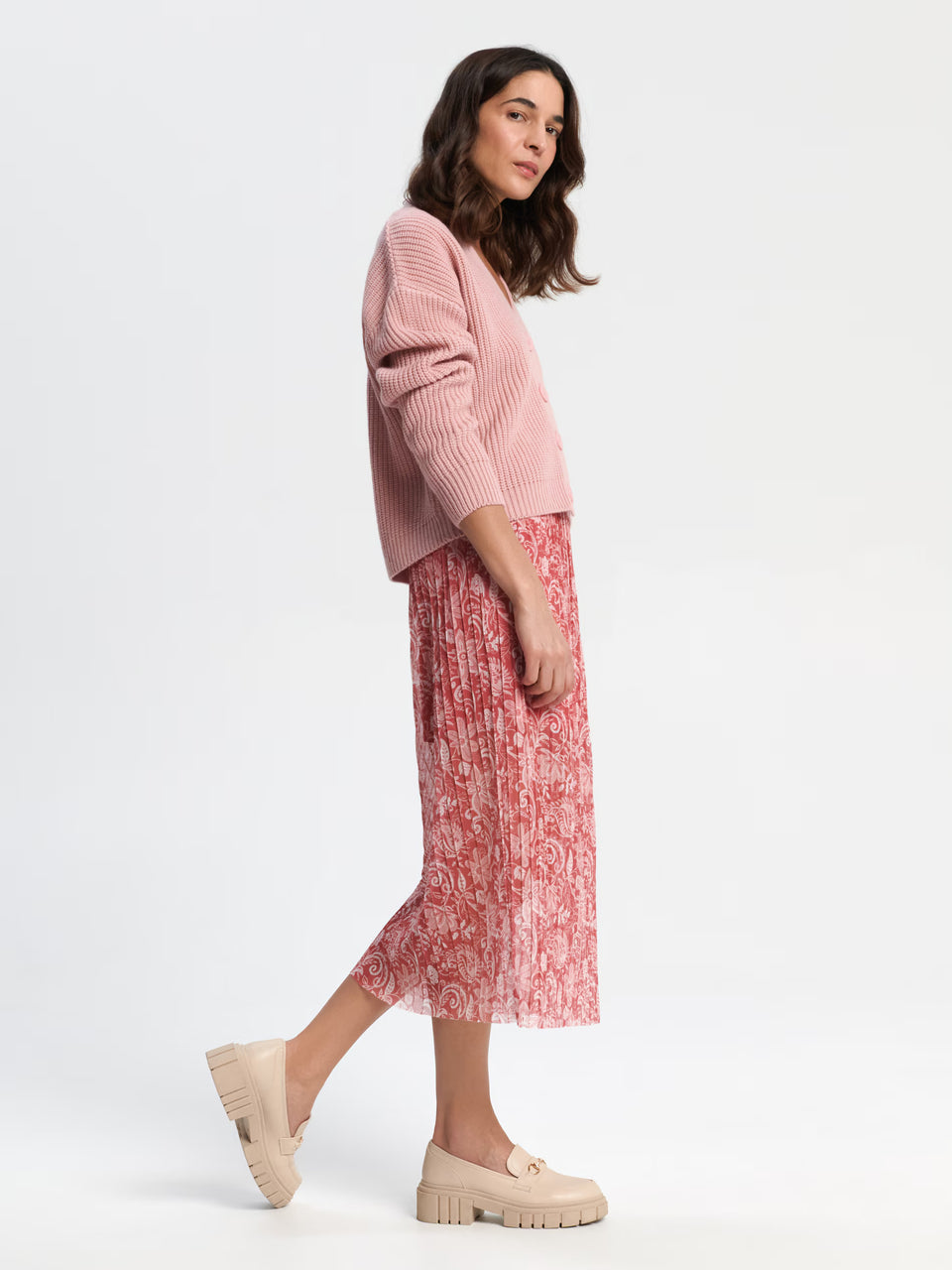 Woman wearing a pink sweater and red patterned skirt on a white background