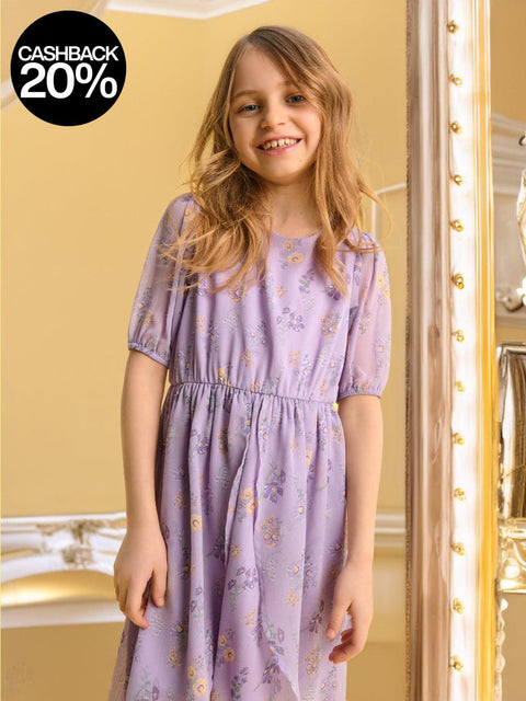 Young girl in a purple floral dress standing in a room with gold accents.