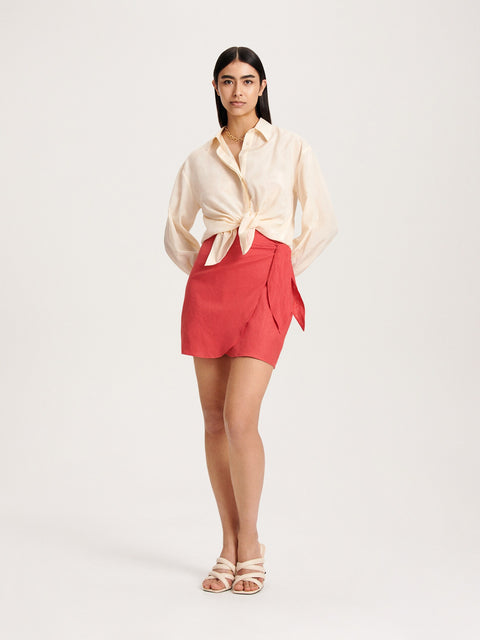 Woman wearing a cream blouse and red skirt on a white background